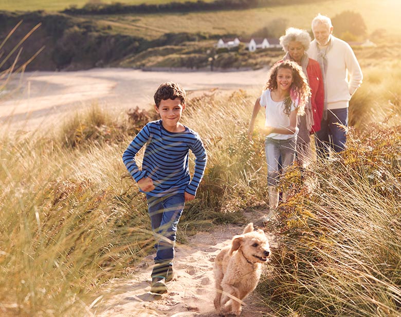 grandson and dog running through sand dunes with his sister and grandparents behind him keep retirement simple
