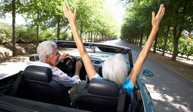 senior couple driving with roof top down serve and protect